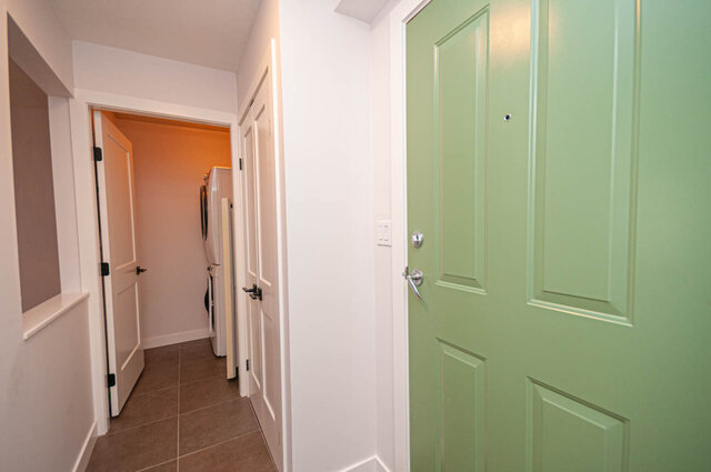 Spacious hallway with mint green door and tiled flooring, leading to a cozy living area. - 313 - 108 West Esplanade Ave, North Vancouver