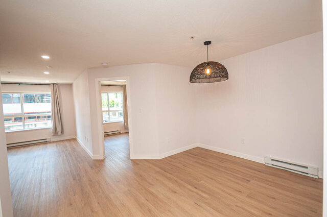Spacious living room with hardwood floors and a modern pendant light. - 313 - 108 West Esplanade Ave, North Vancouver