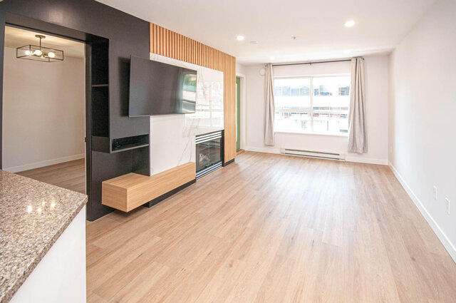 Spacious living room with hardwood floors, modern fireplace, and city view. - 313 - 108 West Esplanade Ave, North Vancouver