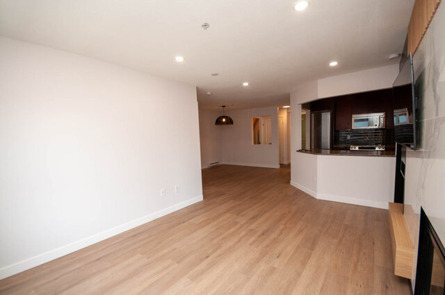 Open-concept living space with hardwood floors and modern kitchen counter. - 313 - 108 West Esplanade Ave, North Vancouver