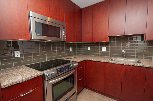 Bright kitchen with granite countertops, stainless steel appliances, and red cabinets. - 313 - 108 West Esplanade Ave, North Vancouver
