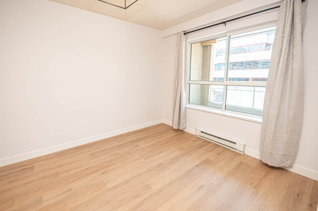 Bright living room with hardwood floors and a large window offering a city view. - 313 - 108 West Esplanade Ave, North Vancouver