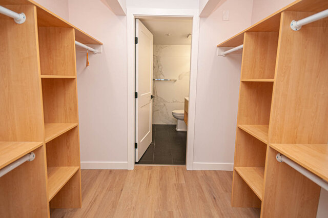 Spacious walk-in closet with wooden shelves and white pipe hangers, leading to a bathroom with marble tiles.