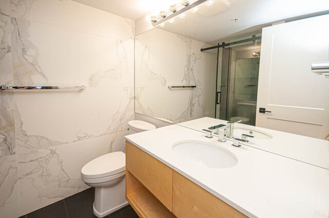Spacious bathroom with marble walls, dual sinks, and a sliding glass shower. - 313 - 108 West Esplanade Ave, North Vancouver