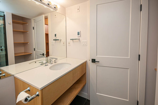 Modern bathroom with dual sinks, light wood cabinets, and a sleek white door. - 313 - 108 West Esplanade Ave, North Vancouver