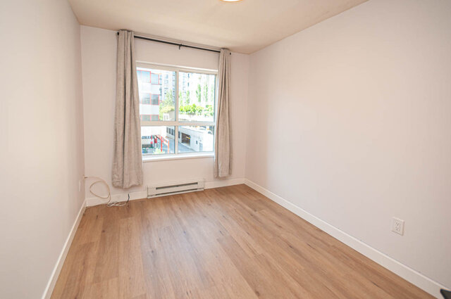 Spacious bedroom with hardwood floors and a city view through the window. - 313 - 108 West Esplanade Ave, North Vancouver