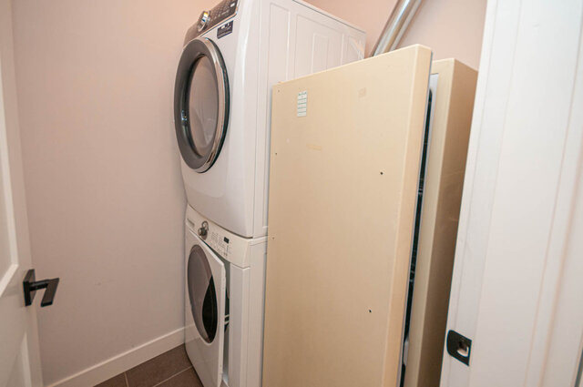 Laundry room with stacked washer and dryer, light-colored cabinets, and tiled floor. - 313 - 108 West Esplanade Ave, North Vancouver
