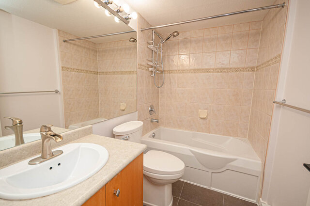 Spacious bathroom with dual sinks, a toilet, and a bathtub/shower combo, featuring light-colored tiles and a modern vanity.