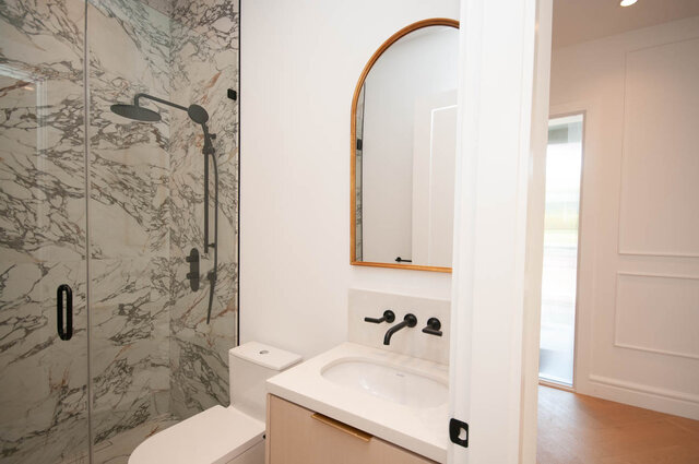 Modern bathroom with marble shower, white countertop, and arched mirror. - Upper - 5909 Athlone St, Vancouver West Side