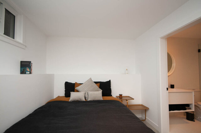 Spacious bedroom with modern white walls, black and white striped pillows, and a cozy reading nook. - 2 - 563 Union Street, Vancouver East Side