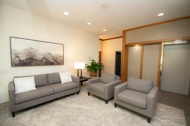 Spacious living room with modern furniture, large abstract art, and a cozy corner with a lamp and plant. - 404 - 1480 Duchess Ave, West Vancouver