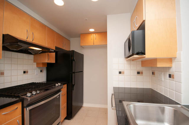 Bright kitchen with wooden cabinets, black appliances, and white tiled backsplash. - 1105 - 198 Aquarius Mews, Vancouver Downtown