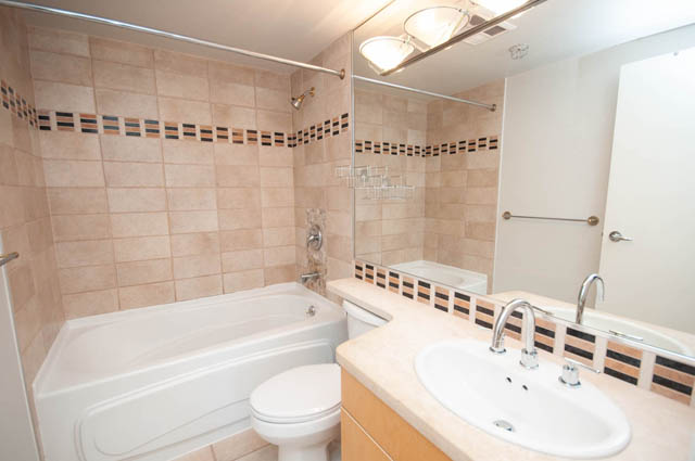 Furnished bathroom with beige tiles, dual sinks, and a large mirror. - 1105 - 198 Aquarius Mews, Vancouver Downtown