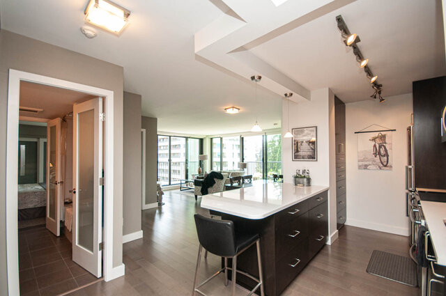 Open-concept kitchen with white countertop island, dark wood cabinetry, and hardwood floors flowing to a bright living room.