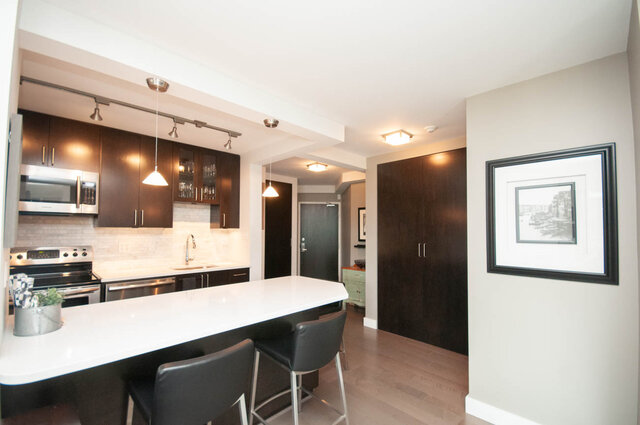 Modern kitchen with dark espresso cabinets, white quartz island, and light hardwood floors. - 1006-4165 Maywood Street, Burnaby