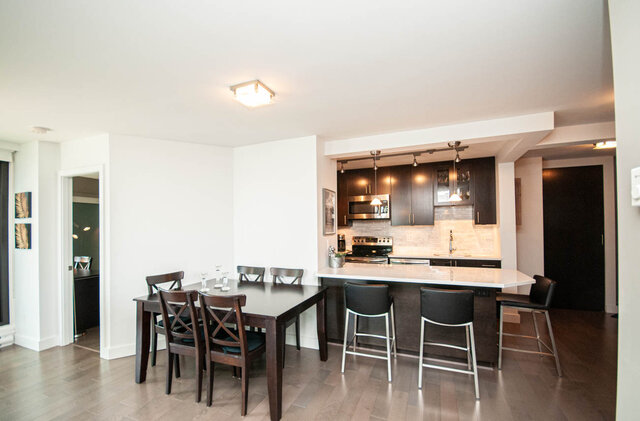 Open dining and kitchen area with dark wood table, white island countertop, and hardwood floors. - 1006-4165 Maywood Street, Burnaby
