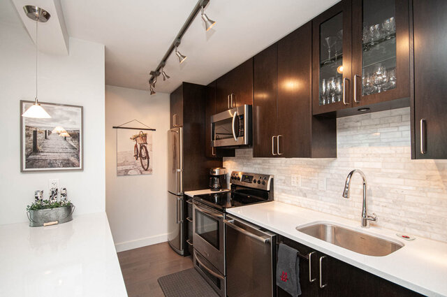 Modern kitchen with dark wood cabinetry, white countertops, stainless steel appliances, and a white subway tile backsplash.