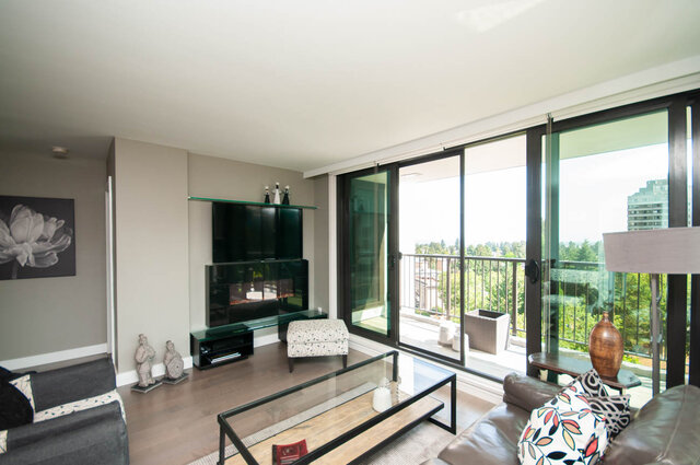 Furnished living room with hardwood floors and sliding glass doors opening to a balcony with a green city view. - 1006-4165 Maywood Street, Burnaby