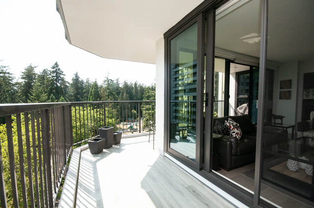 Spacious balcony with forest view and sliding glass doors opening to a furnished living room. - 1006-4165 Maywood Street, Burnaby