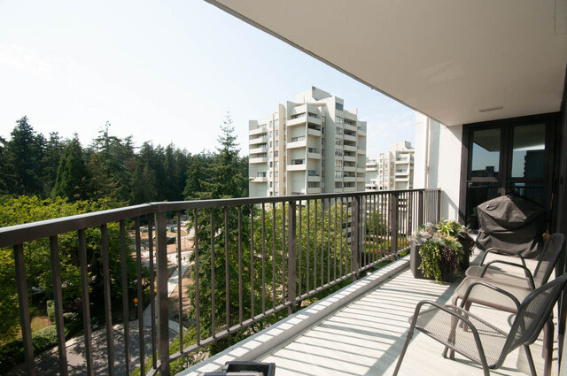 Balcony with metal railing and mesh chairs overlooking lush trees and a high-rise building. - 1006-4165 Maywood Street, Burnaby
