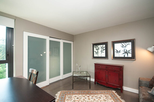 Furnished living room with hardwood floors, a red cabinet, framed bamboo art, and frosted glass sliding doors. - 1006-4165 Maywood Street, Burnaby