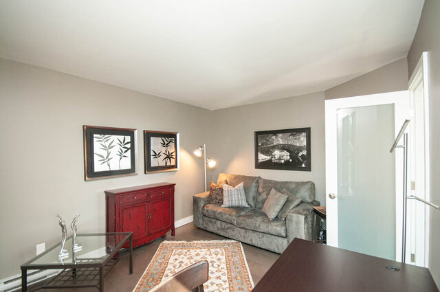 Furnished living room with grey velvet sofa, red sideboard, and patterned area rug. - 1006-4165 Maywood Street, Burnaby