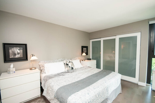 Furnished bedroom with a made bed, white nightstands, and frosted glass sliding closet doors. - 1006-4165 Maywood Street, Burnaby
