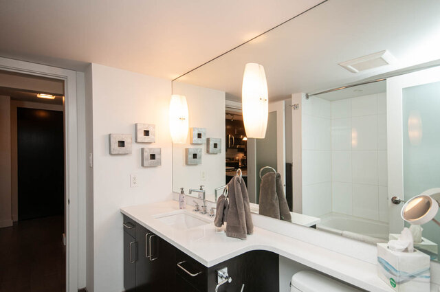 Modern bathroom vanity with white countertop, dark cabinetry, and a glass-enclosed shower. - 1006-4165 Maywood Street, Burnaby