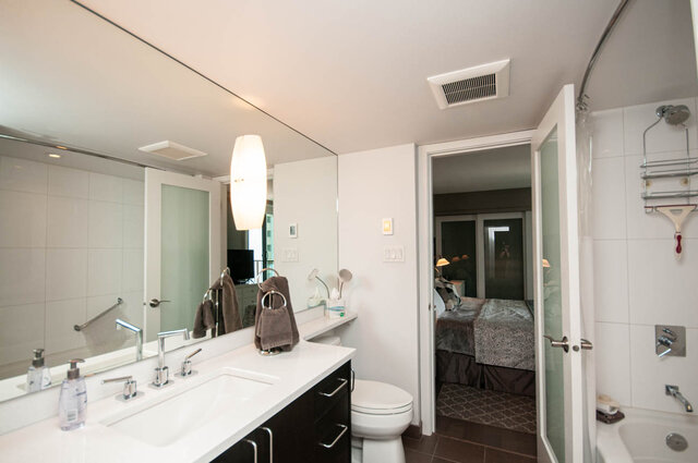 Modern bathroom with white countertops, dark vanity cabinets, and a large wall mirror. - 1006-4165 Maywood Street, Burnaby