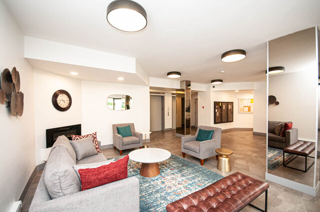 Furnished living room with grey sofas, red and teal pillows, a marble coffee table, and a tufted leather bench. - 1006-4165 Maywood Street, Burnaby