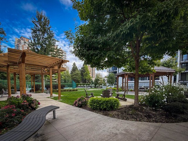 Outdoor courtyard with wooden pergola, curved bench, and landscaped flower beds beside a lawn seating area. - 1006-4165 Maywood Street, Burnaby