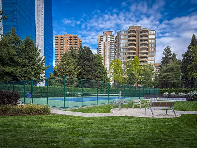 Lush outdoor courtyard with a fenced tennis court and bench seating overlooking high-rise condos. - 1006-4165 Maywood Street, Burnaby