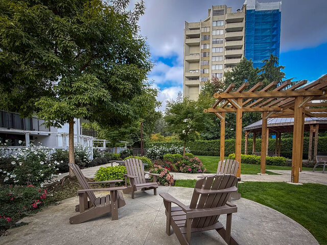 Outdoor courtyard with wooden Adirondack chairs and a pergola overlooking a flowering garden and high-rise view. - 1006-4165 Maywood Street, Burnaby