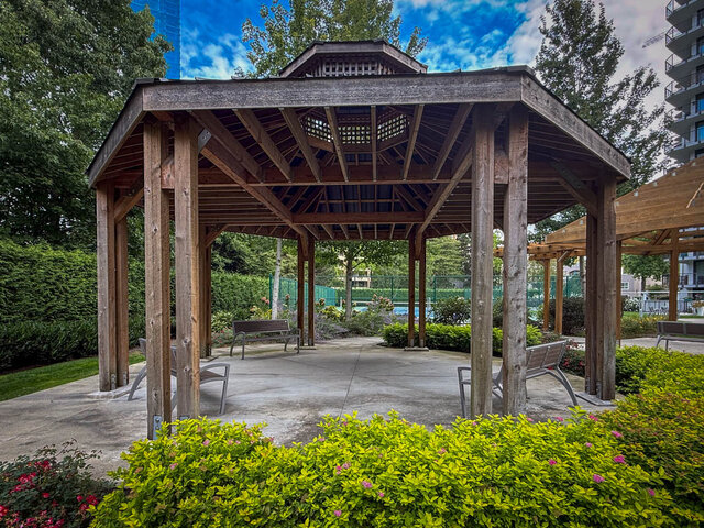 Wooden pergola pavilion with concrete patio, slat benches, and landscaped greenery in a shared outdoor courtyard. - 1006-4165 Maywood Street, Burnaby