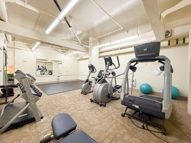 In-unit fitness room with treadmills, ellipticals, and dumbbells on patterned carpet flooring. - 1006-4165 Maywood Street, Burnaby