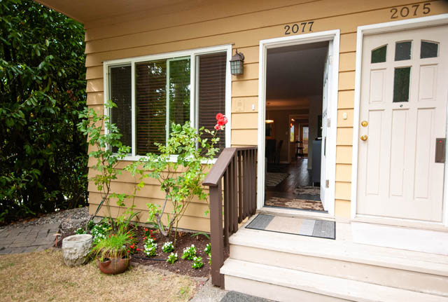 Furnished living room with sliding glass door leading to a patio, surrounded by greenery. - 2077 W 13th Ave, Vancouver West Side