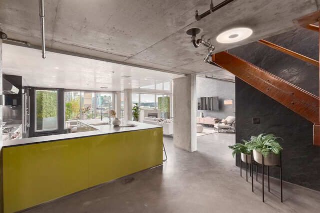 Open kitchen with a lime-green island, polished concrete floors, and a city view through floor-to-ceiling windows.