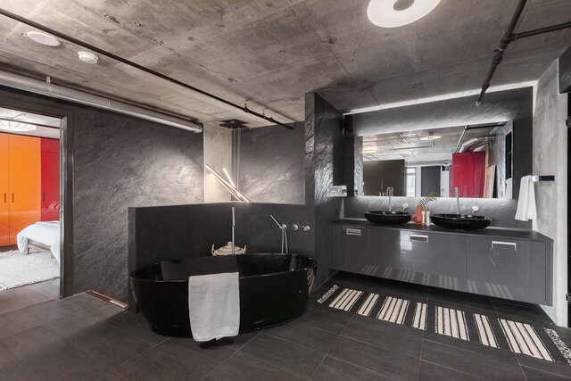 Industrial bathroom with black freestanding tub, dark marble walls, and double vanity with vessel sinks.
