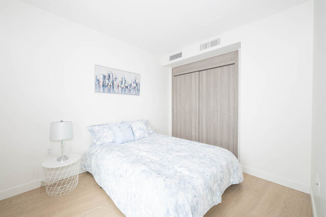 Bright bedroom with light blue floral bed linens, white wire nightstand, and cityscape wall art. - 2204 - 89 Nelson Street, Vancouver Downtown