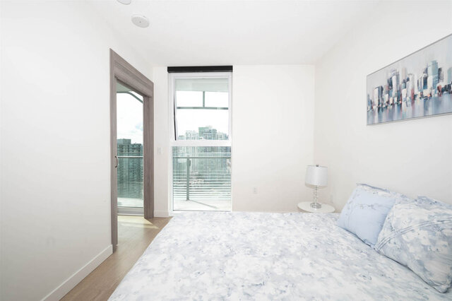 Spacious bedroom with city view through large windows and light blue floral bedding. - 2204 - 89 Nelson Street, Vancouver Downtown