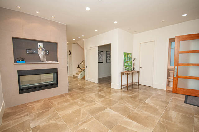 Spacious living room with modern fireplace, glossy tile floors, and open layout. - 4504 West 12th Ave, Vancouver West Side