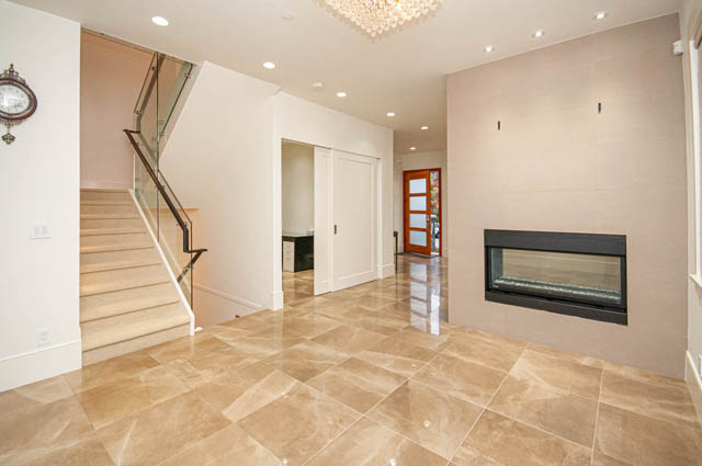 Spacious entryway with modern fireplace, glass rail staircase, and glossy tile floors. - 4504 West 12th Ave, Vancouver West Side