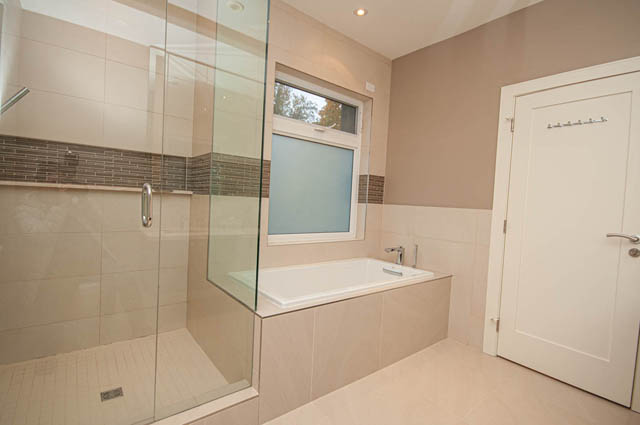 Spacious bathroom with modern fixtures, large glass shower, and neutral tile walls. - 4504 West 12th Ave, Vancouver West Side