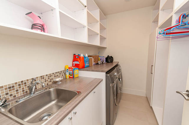 Efficient laundry room with ample storage, modern sink, and colorful hangers. - 4504 West 12th Ave, Vancouver West Side