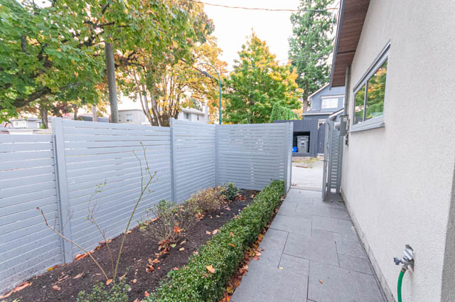 Fenced backyard with modern grey slats and paved pathway leading to a house entrance. - 4504 West 12th Ave, Vancouver West Side