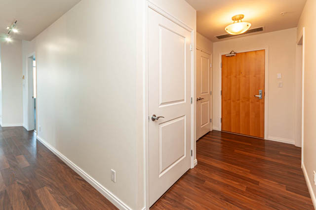 Bright hallway with hardwood floors and white walls leading to a wooden door. - 3102 - 1211 Melville Street, Vancouver Downtown