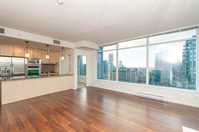 Bright living room with hardwood floors and city view, modern kitchen with stainless steel appliances.