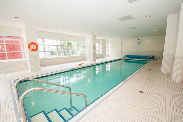 Spacious indoor pool area with tiled walls and floor, large windows, and a blue pool deck. - 3102 - 1211 Melville Street, Vancouver Downtown