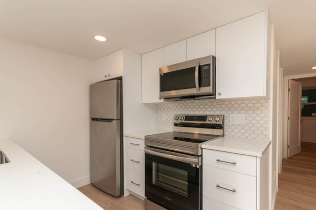 Bright kitchen with white cabinets, stainless steel appliances, and geometric tile backsplash. - Suite - 778 Crystal Court, North Vancouver