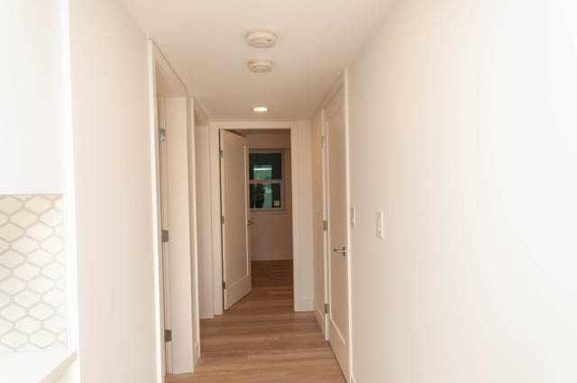 Spacious hallway with white walls, wooden floors, and a view of another room at the end. - Suite - 778 Crystal Court, North Vancouver